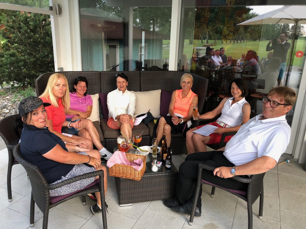 Gruppe von Golferinnen und Golfern im Golfclub-Clubhaus: entspannte After-Golf-Runde auf der Terrasse mit Getränken