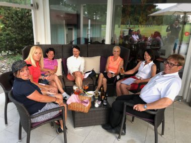 Gruppe von Golferinnen und Golfern im Golfclub-Clubhaus: entspannte After-Golf-Runde auf der Terrasse mit Getränken