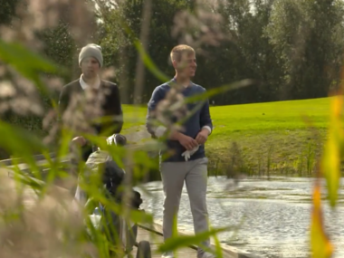 Zwei Golfer auf Brücke am Teich, grüner Golfplatz in der Natur bei Sonne