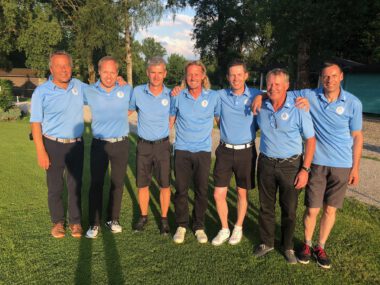 Herren-Golfteam im Gruppenfoto auf dem Golfplatz, Spieler in blauen Poloshirts lächeln in der Abendsonne