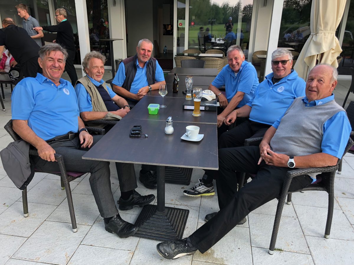 Golfteam-Gruppenfoto: Herren in blauen Poloshirts entspannen nach dem Turnier auf der Clubhaus-Terrasse