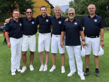 Golfteam: sechs Männer in navy-blauen Poloshirts und weißen Shorts posieren lächelnd auf dem Golfplatz