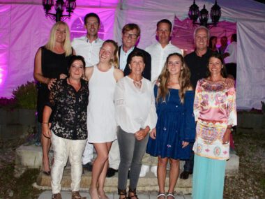 Gruppenfoto bei Gartenparty vor Zelt mit lila Licht, festliche Kleidung, lächelnde Gäste am Abend.