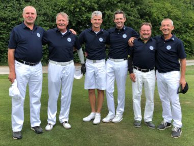 Golfteam im Gruppenfoto: sechs Golfer in dunkelblauen Polos und weißen Hosen auf dem Golfplatz, lächelnd.