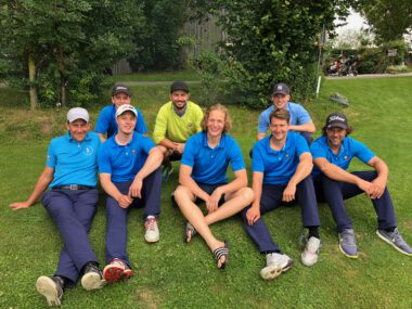 Golfteam in blauen Poloshirts sitzt auf Rasen am Golfplatz – Mannschaftsfoto, Outdoor-Sport, Teamgeist