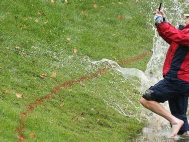 Golfer barfuß schlägt Ball aus Wasserhindernis, großer Splash am grünen Golfplatz.