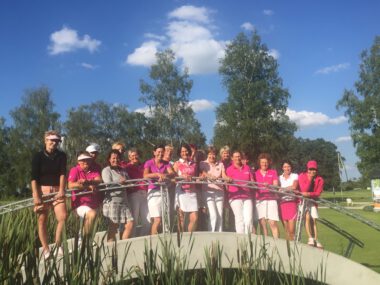 Damen-Golfteam in Pink auf Brücke – Gruppenfoto am sonnigen Golfplatz bei blauem Himmel und Bäumen