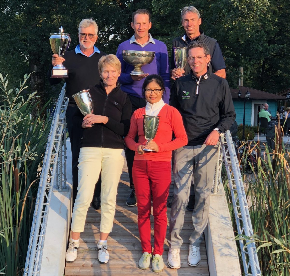 Gruppenfoto: Golfturnier-Siegerteam mit Pokalen auf Holzbrücke im Grünen