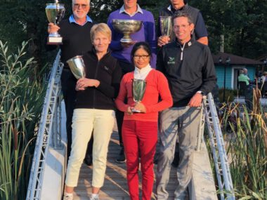 Gruppenfoto: Golfturnier-Siegerteam mit Pokalen auf Holzbrücke im Grünen