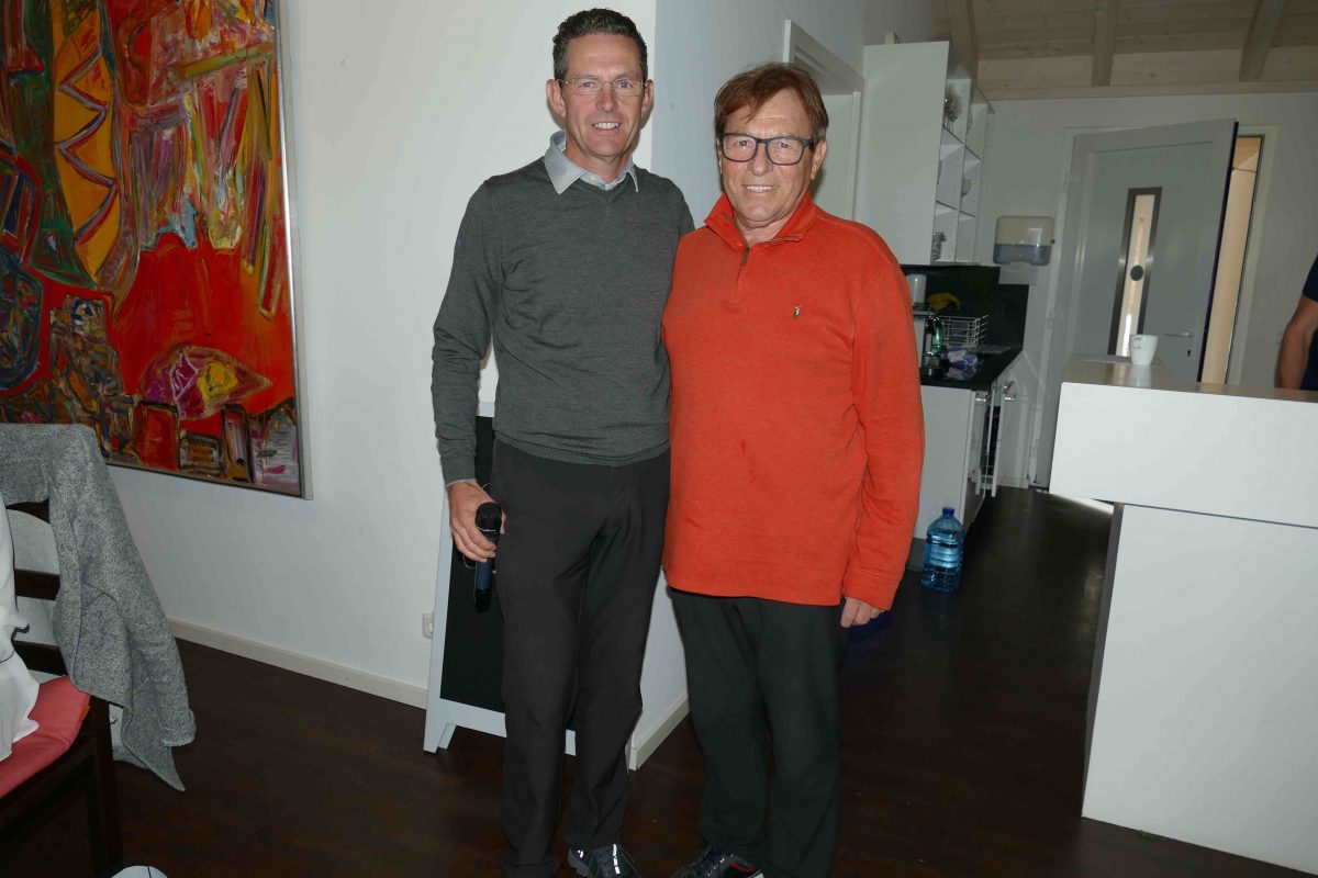 Zwei Männer lächeln in moderner Wohnküche; einer hält Mikrofon, Kunstbild im Hintergrund, Porträtfoto indoor