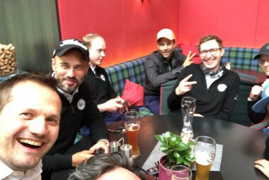 Gruppe Männer beim After-Work in Bar: Selfie mit Biergläsern, lockere Stimmung, Teamtreffen, gesellige Runde.