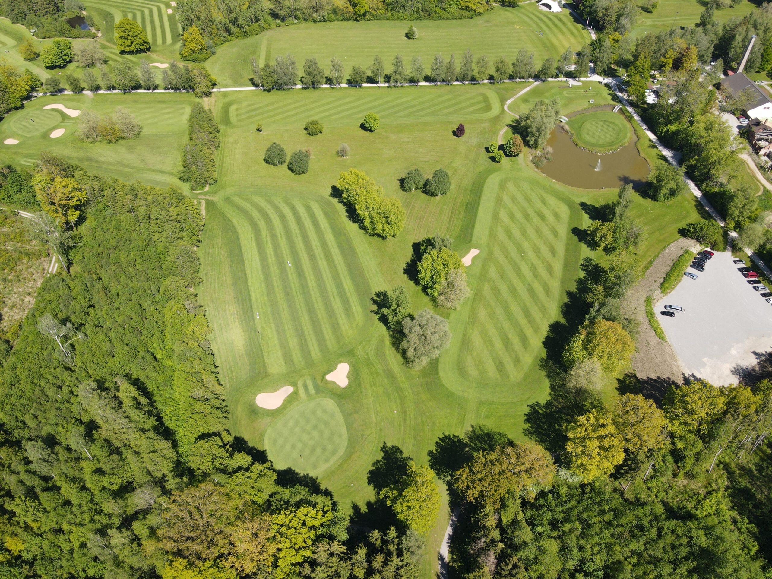 Golfplatz Luftaufnahme mit gepflegten Fairways, Greens, Bunkern und Wasserhindernis in grüner Landschaft