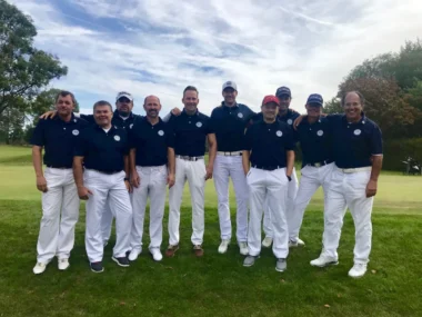Teamfoto zehnköpfiges Herren-Golfteam in dunkelblauen Poloshirts und weißen Hosen auf dem Grün des Golfplatzes