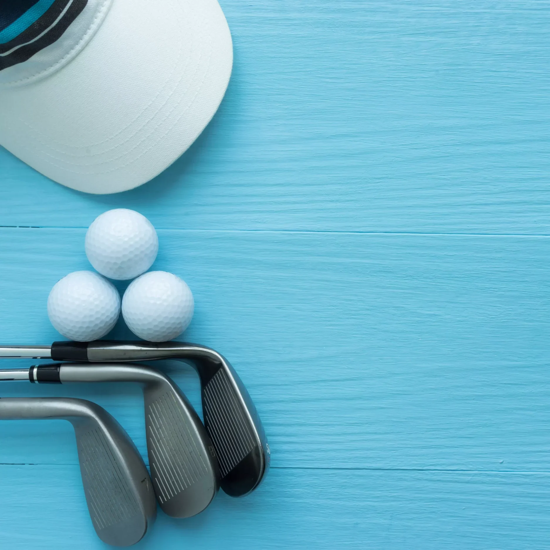 Golf-Ausrüstung: Golfschläger, drei Golfbälle und weiße Kappe auf blauem Holzhintergrund, Flatlay