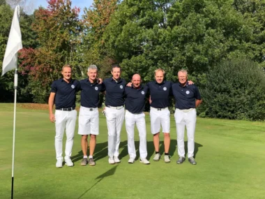 Herren-Golfteam posiert zu sechst auf dem Green neben Fahne – Gruppenfoto auf dem Golfplatz bei Sonne