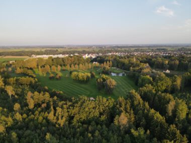 Drohnenaufnahme Parklandschaft mit Teich und Wiesen, umgeben von Wald, nahe Dorf im Abendlicht