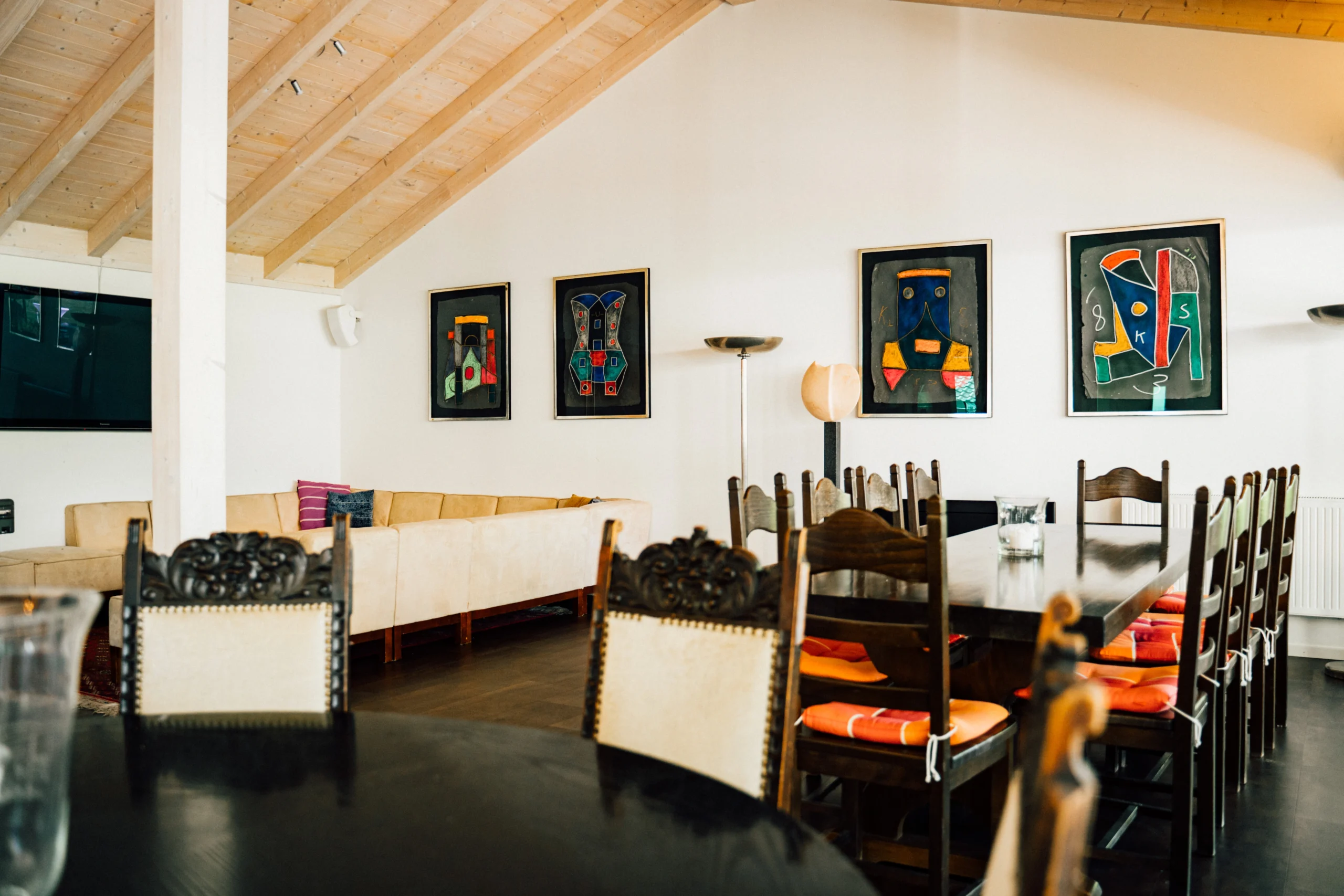 Modernes Esszimmer mit langer Holztafel, rustikalen Stühlen, orangen Kissen und abstrakter Kunst an weißer Wand