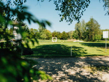 Golfplatz in Parklandschaft bei Sonnenschein mit Teich, kleiner Brücke und runder Steinskulptur – ruhige Naturidylle