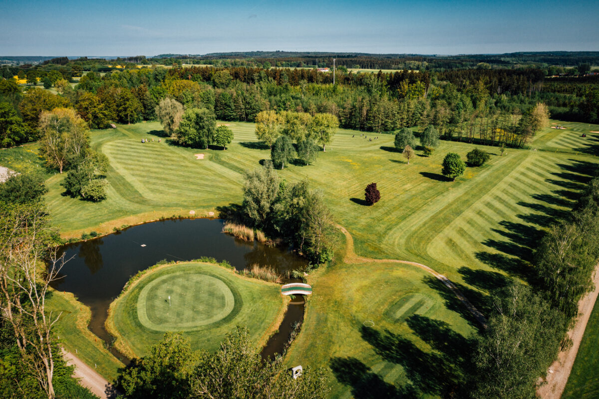 Luftaufnahme Golfplatz mit Green, Fairways, Teich und Brücke in grüner Landschaft