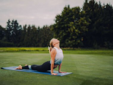 Yoga im Freien: Johanna Specht in Kobra-Pose auf Yogamatte, Rückendehnung und Entspannung auf grüner Wiese.